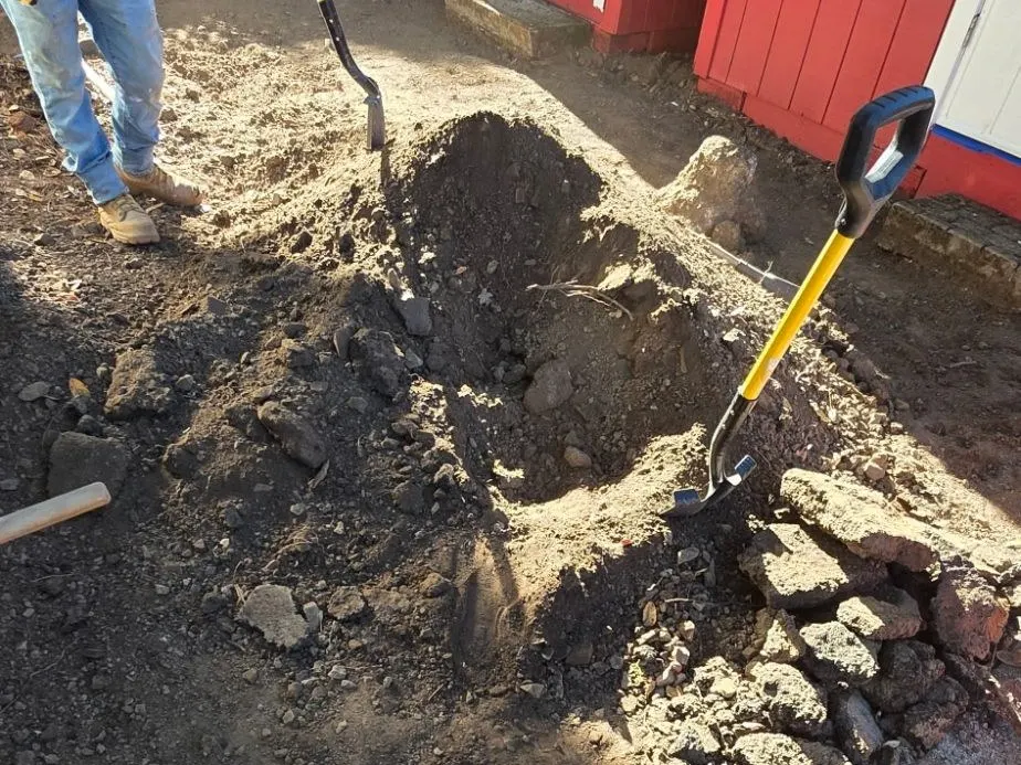 Old soil and rock dug out next to a red shed before a paver base goes in