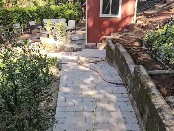 New gray paver walkway running along a low stone wall up to a red garden shed
